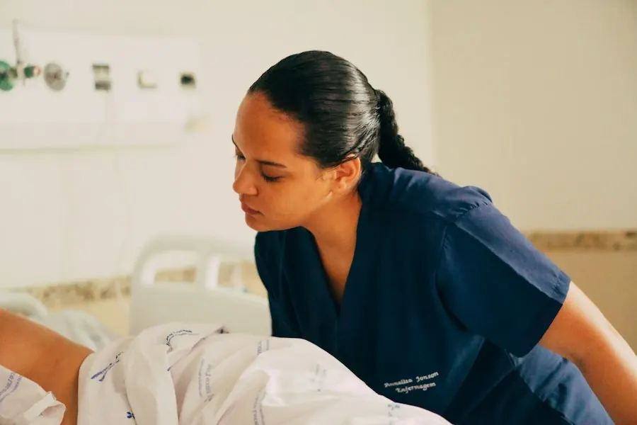 A nurse in navy scrubs leans over a patient's bed