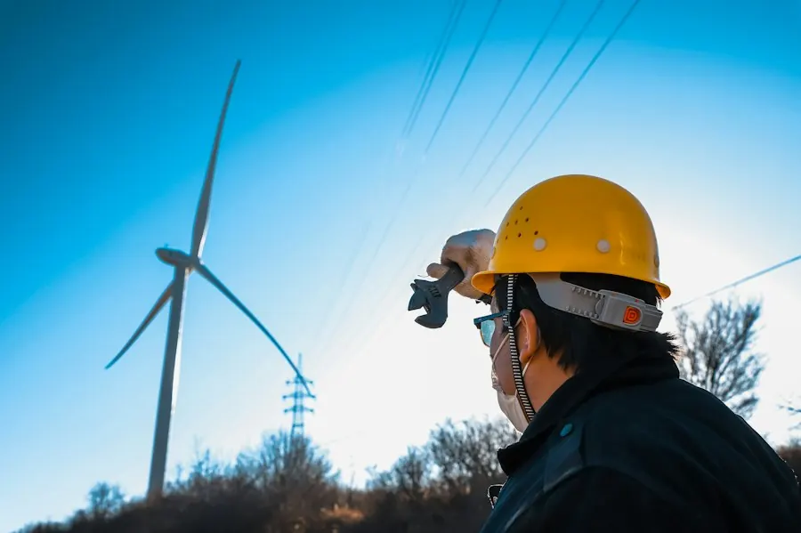 A technician in a yellow hard hat looks up at a wind turbine